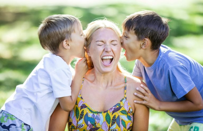 Two young boys shouting in mother's ears outdoors